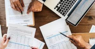 Looking on from above to a group of three individuals discussing reports on paper and the computer.