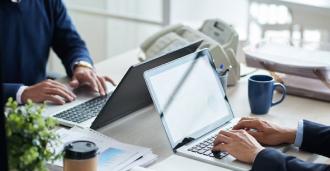 Two individuals doing work on their laptops at a desk.